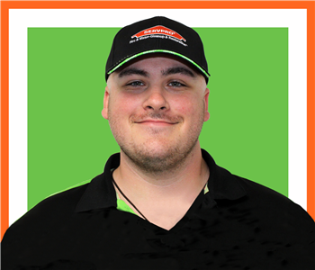 male employee wearing servpro hat and standing under green SERVPRO sign