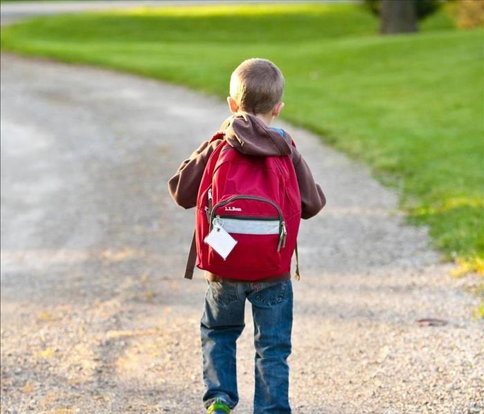 young boy walks down road with backpack