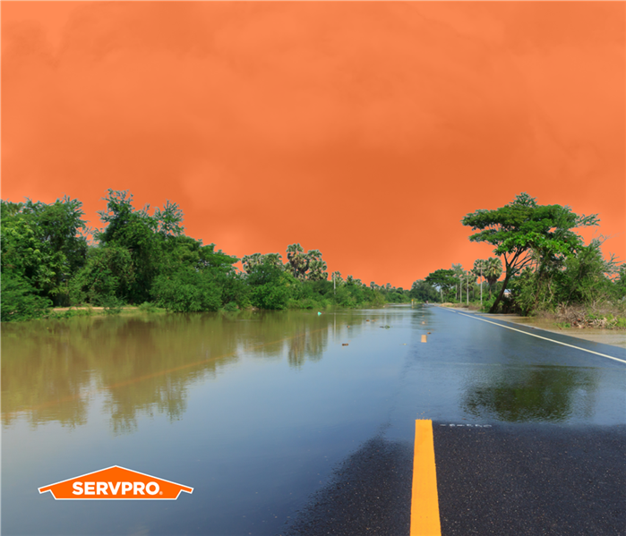 Flood waters over a 2 lane road, orange sky, servpro logo in corner, treeline on horizon